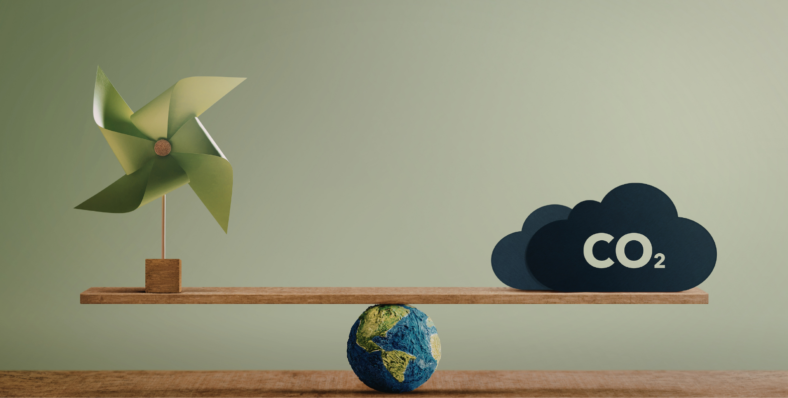 Wippe aus Holz auf einer Weltkugel, links ein kleines Windrad aus Papier, rechts eine Wolke mit der Aufschrift „CO₂“.
