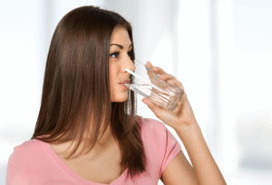 Frau trinkt Wasser aus einem Glas zuhause