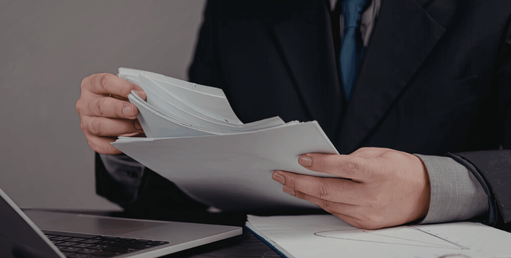 Eine Person sitzt an einem Laptop, Rechnungen in der Hand.